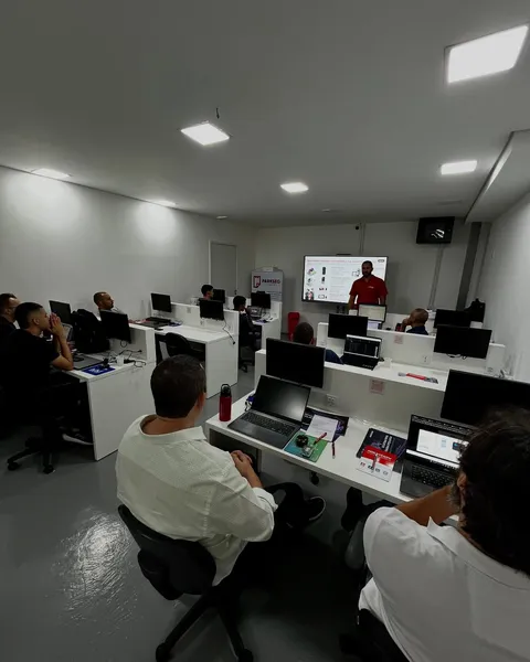Alunos acompanhando o instrutor na sala de treinamento, com notebooks e monitores nas bancadas